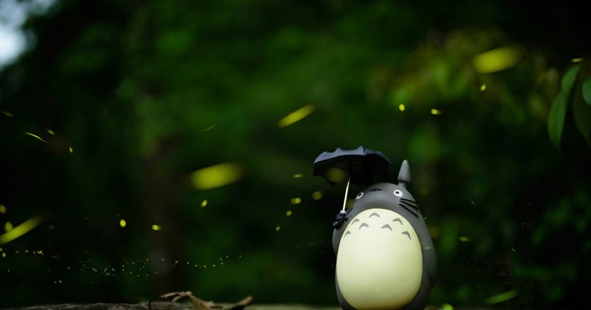 トトロのフィギュアと蛍が飛び交う緑の森の風景